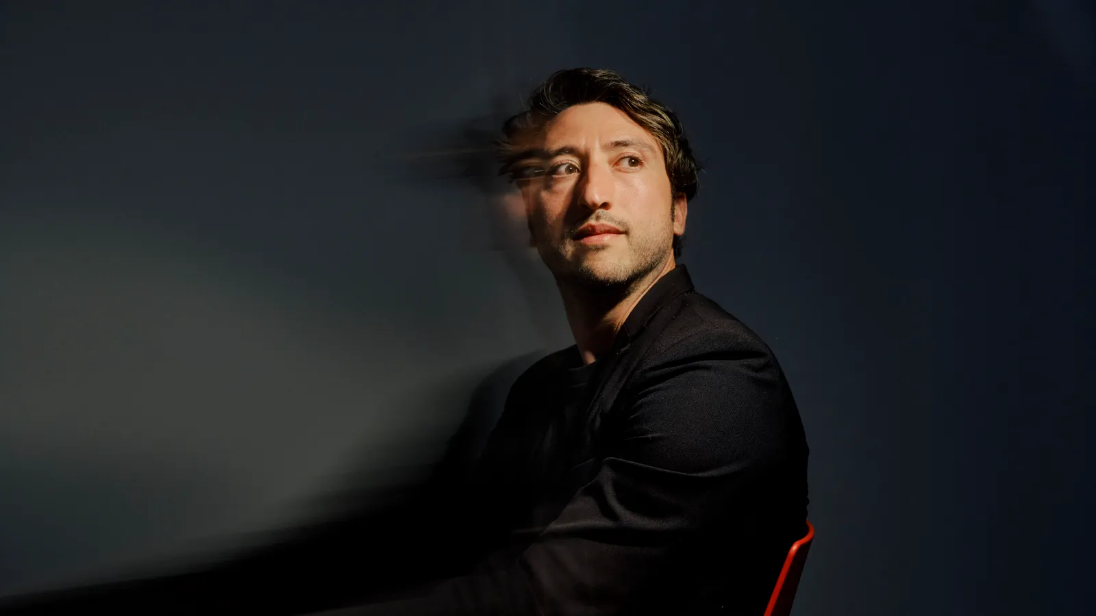 Marcello Ienca in a black suit, seated against a dark background with a motion blur effect.